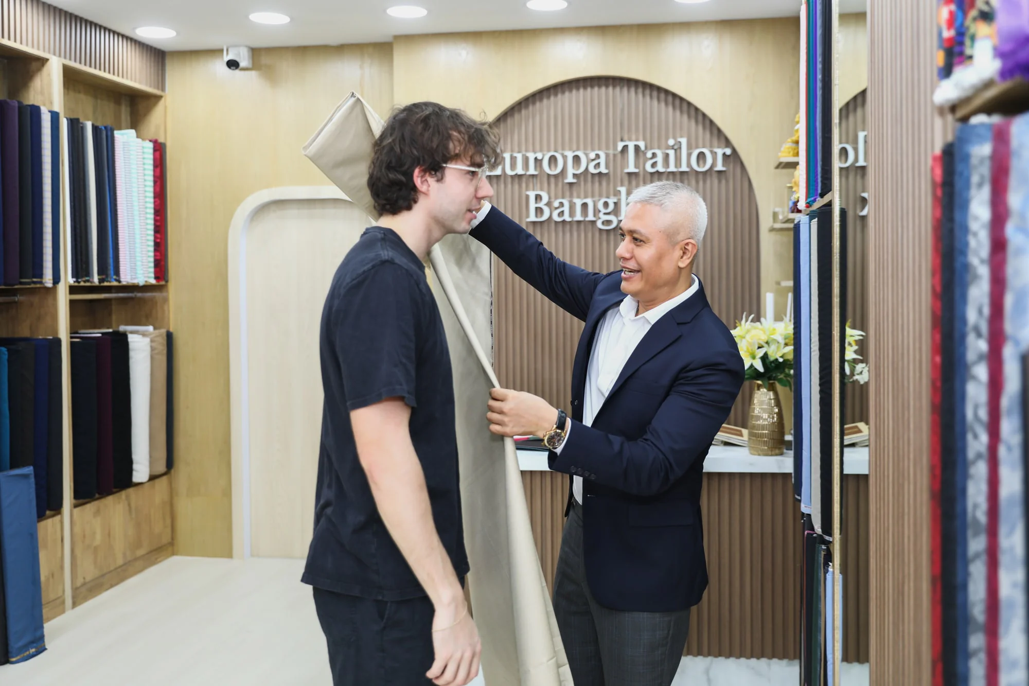 Jack draping beige cloth over a client’s shoulder to assess its fall